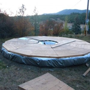 Yurt platform, silver edition. Leveled ground, tamped gravel, tarp, strawbales, tarp folded on top of bales & taped with tyvek to seal, platform wedge