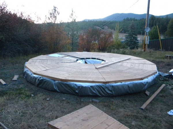 Yurt platform, silver edition. Leveled ground, tamped gravel, tarp, strawbales, tarp folded on top of bales & taped with tyvek to seal, platform wedge